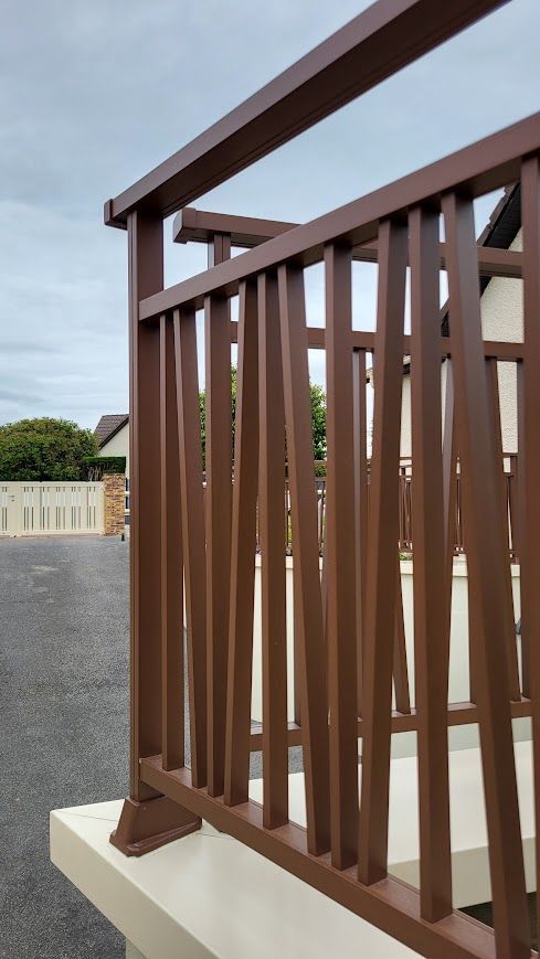 Rambarde en métal brun à barres verticales sur une base en béton blanc, vue extérieure.