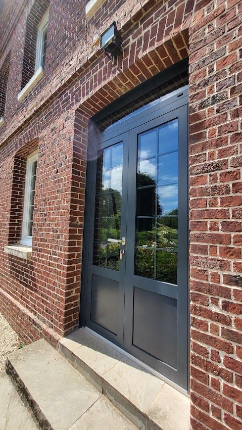 Façade en briques avec double porte grise et panneaux de verre.