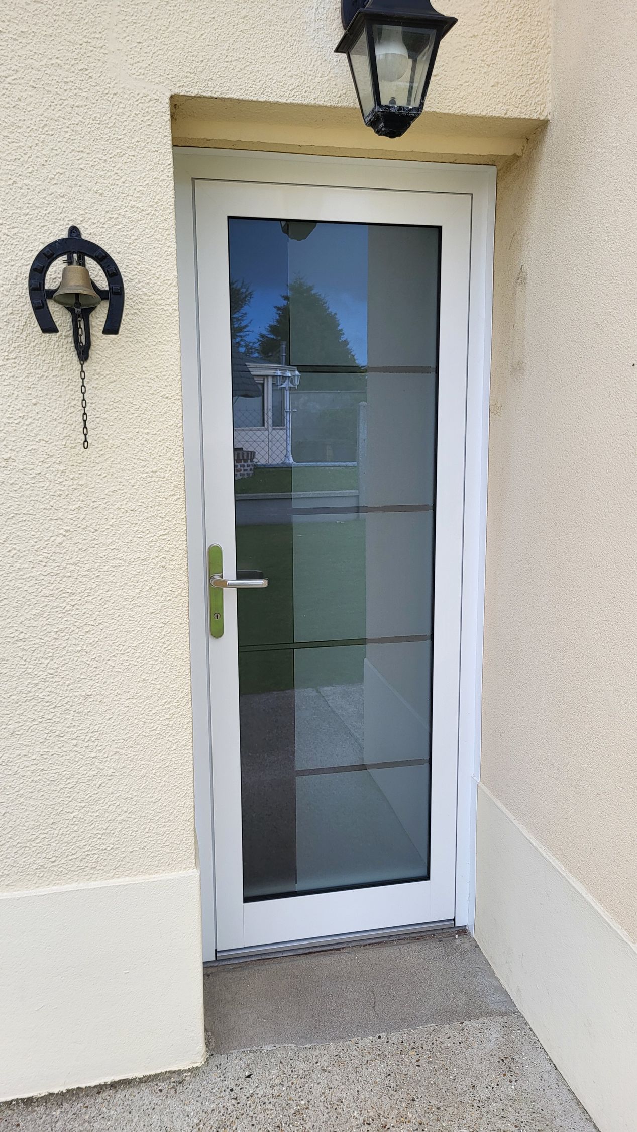 Porte d'entrée blanche avec panneaux de verre ; vue extérieure, sonnette et applique murale.