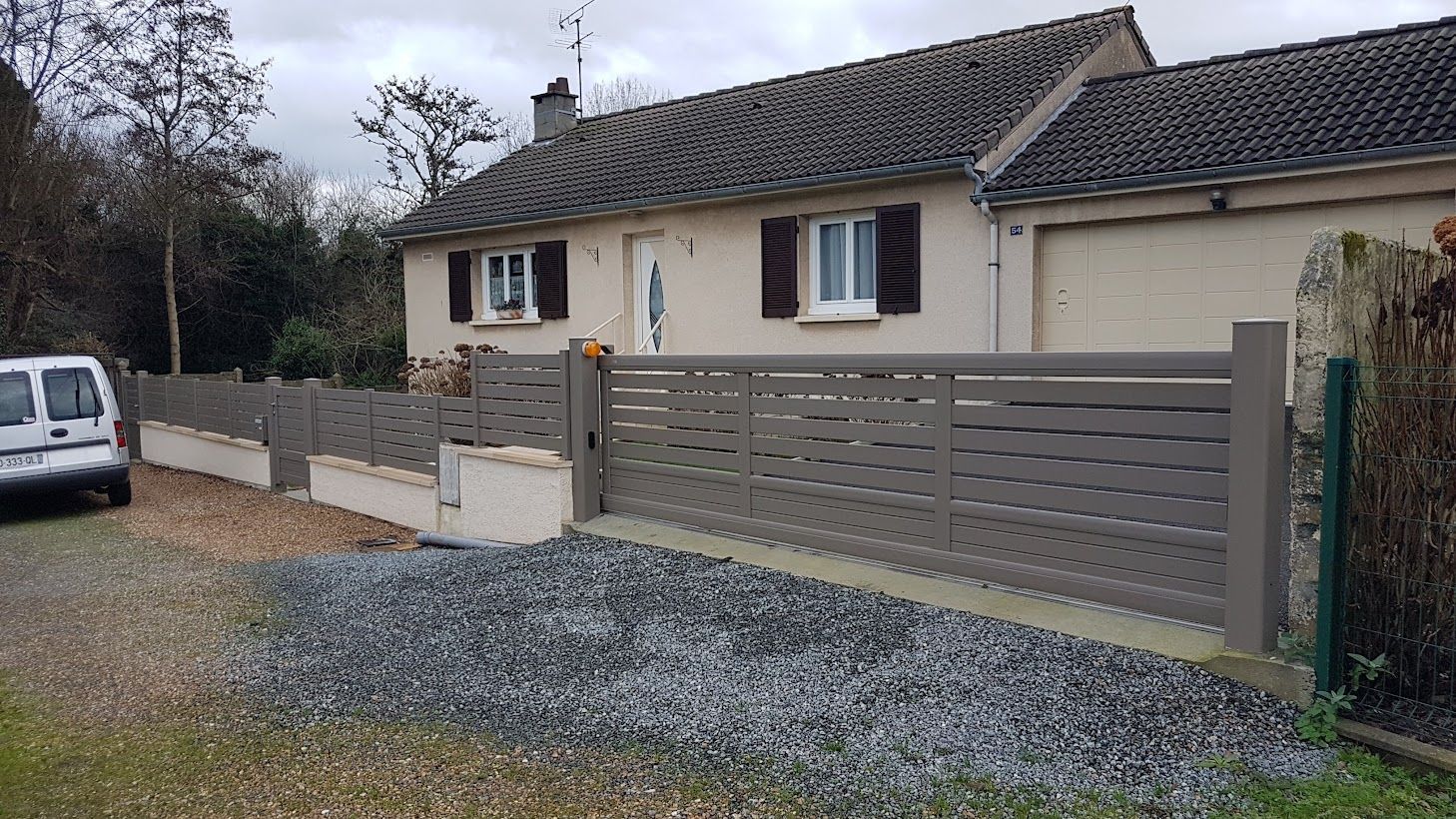 Maison grise avec clôture et portail assortis ; allée en gravier.