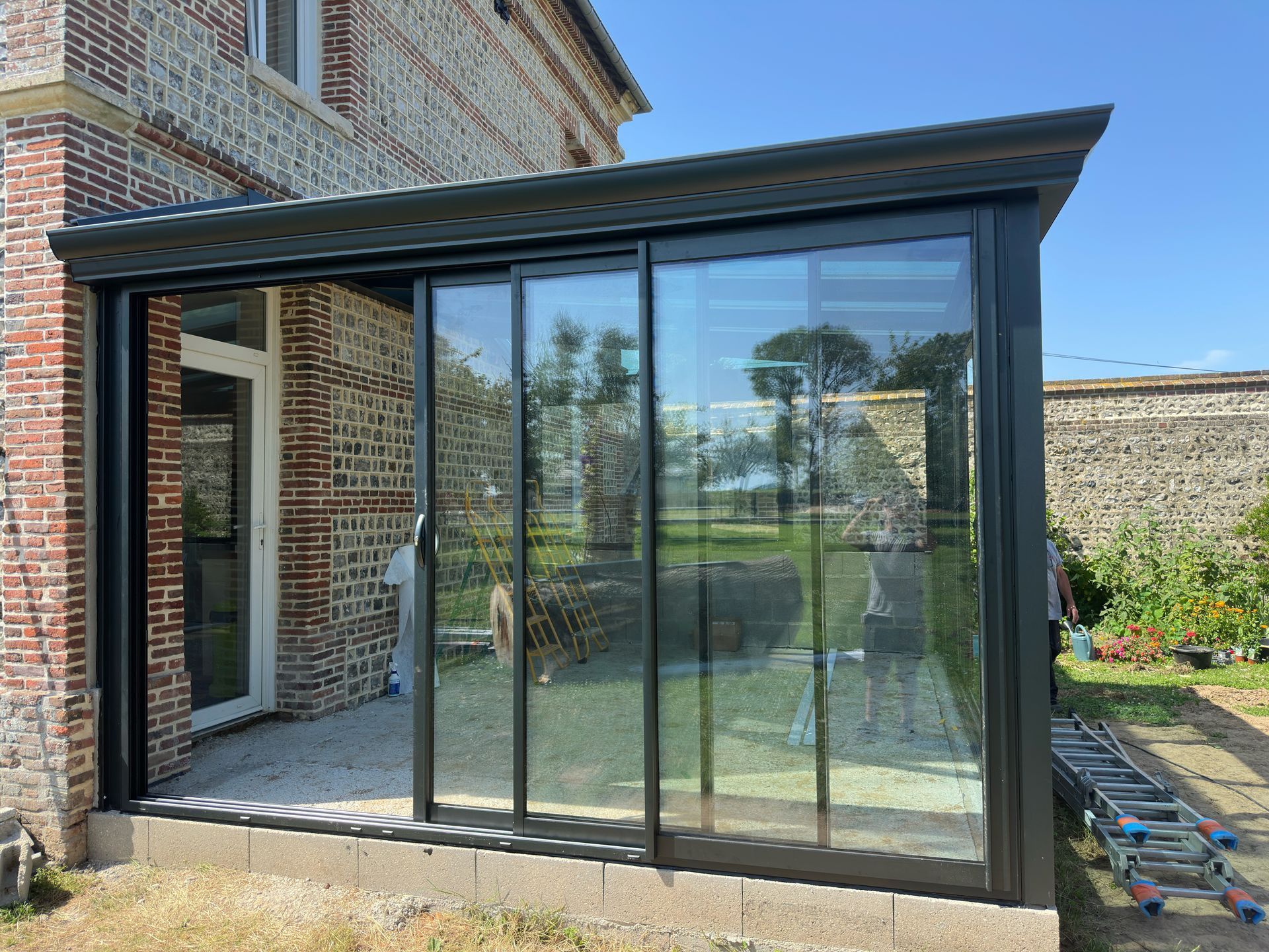 Portes coulissantes en verre à cadre noir donnant sur le patio d'une maison en briques. Un jardin se trouve en arrière-plan.