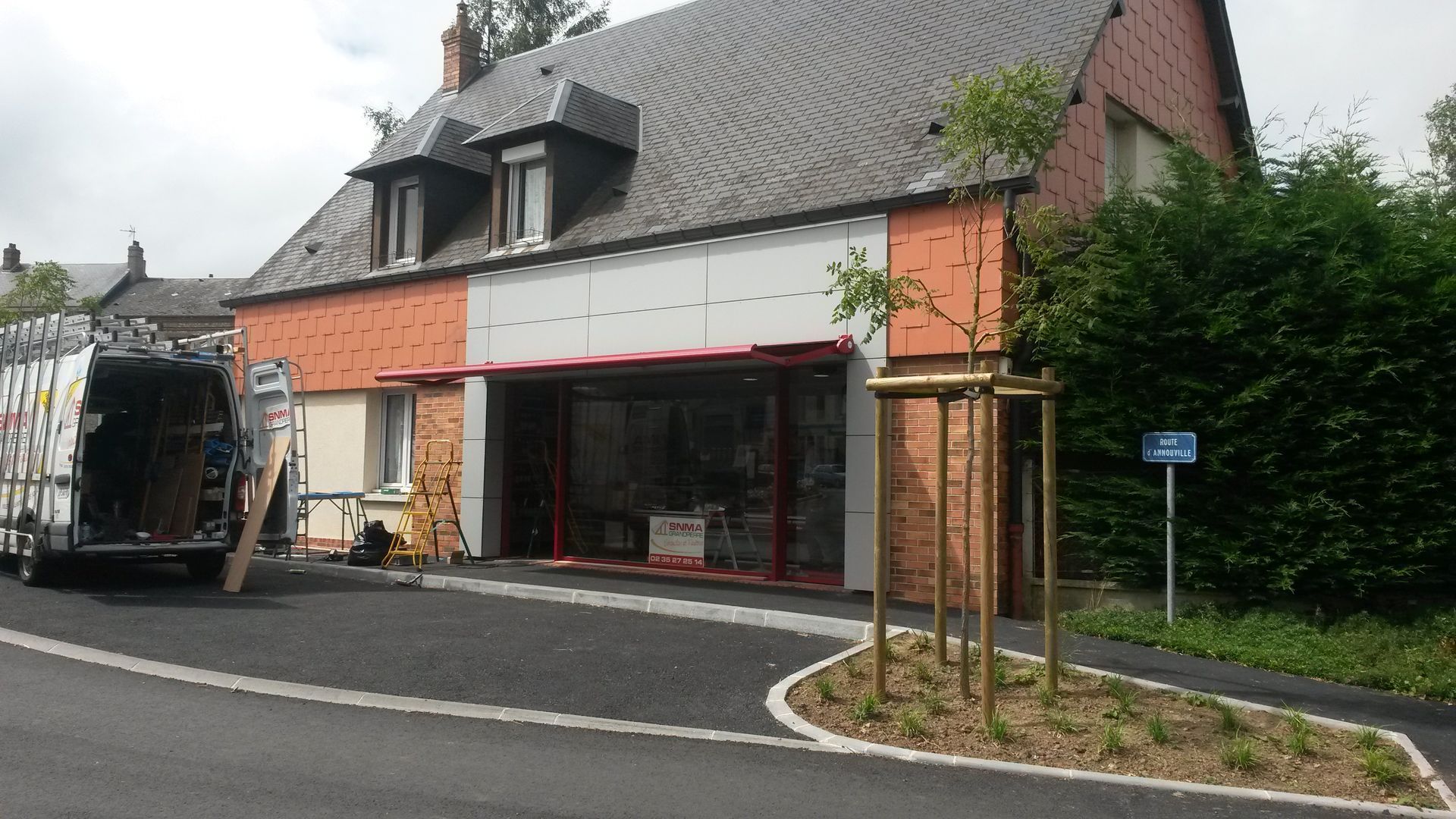 Un bâtiment en rénovation, avec une camionnette garée devant. Le bâtiment présente des parties orange et blanches.