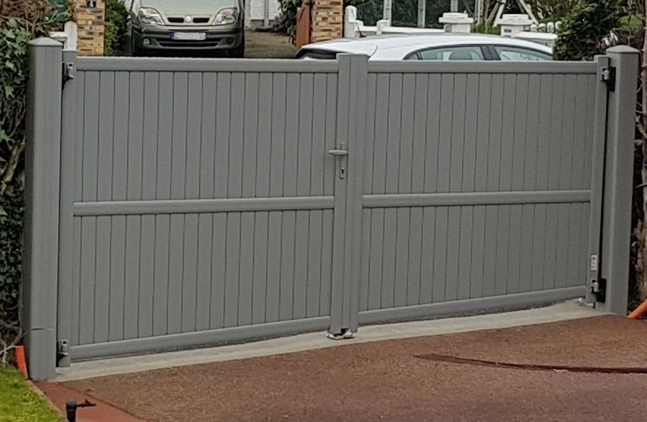 Portail gris à double battant devant une allée, avec des voitures visibles derrière.