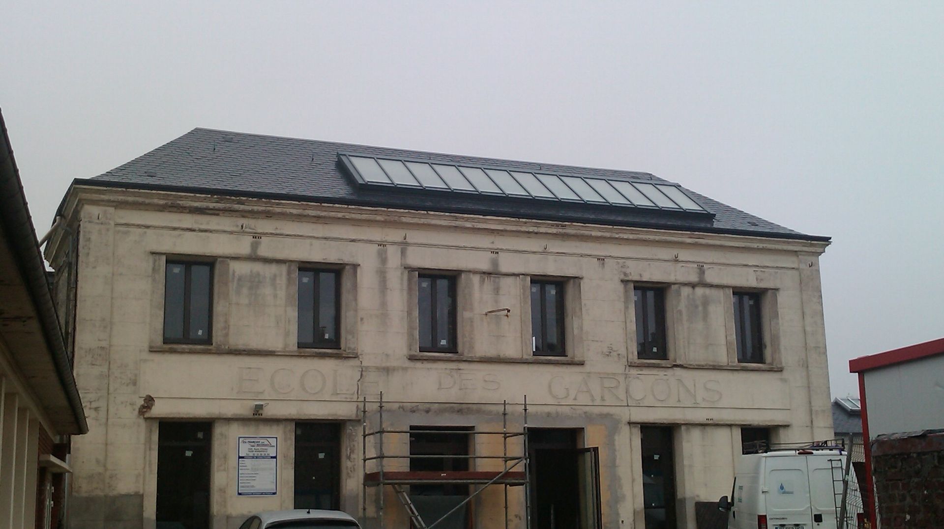Bâtiment de deux étages avec panneaux solaires sur le toit. Le nom MAIRIE est visible sur la façade, sous un ciel nuageux.