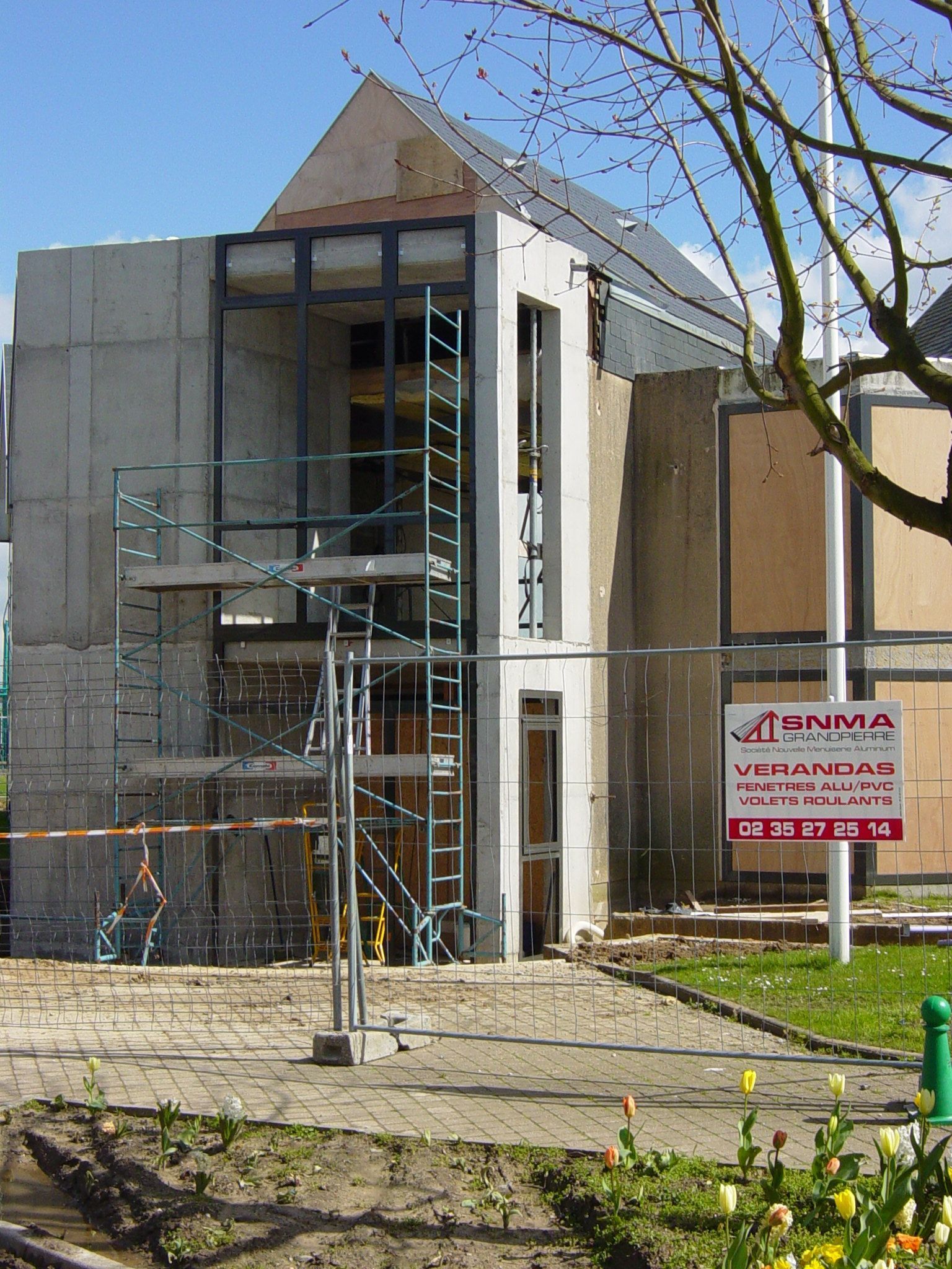 Bâtiment en construction avec échafaudages et panneau. Tons de béton et de gris.