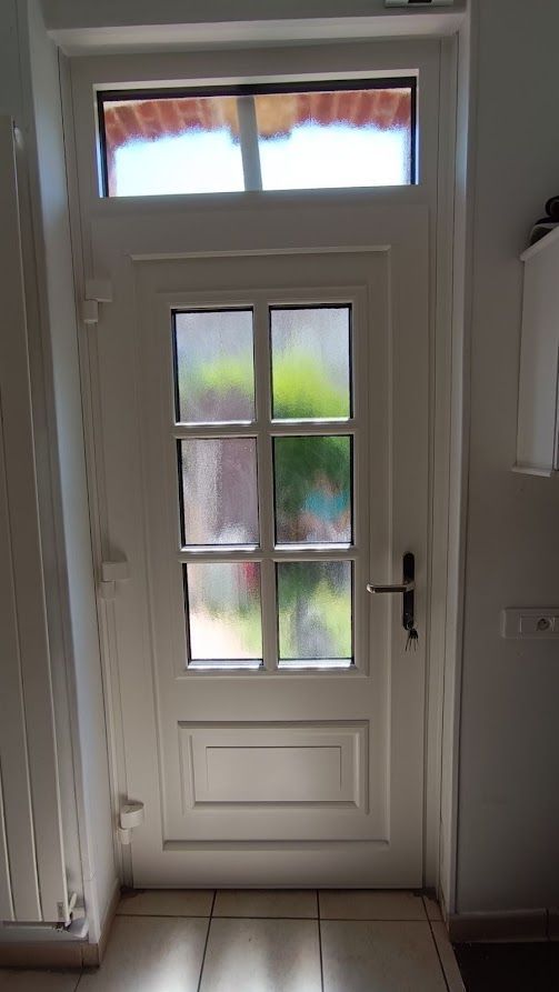 Porte blanche à six carreaux et imposte, donnant sur une vue extérieure floue.