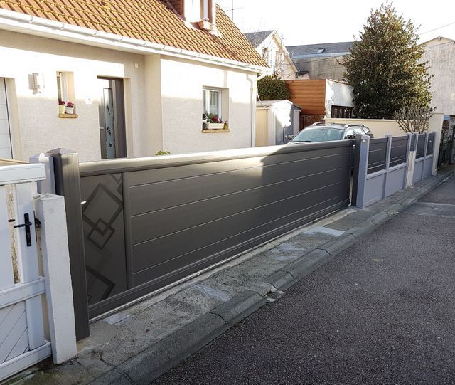 Portail coulissant gris devant une maison, orné d'un motif décoratif en losanges, posé sur un trottoir en béton.