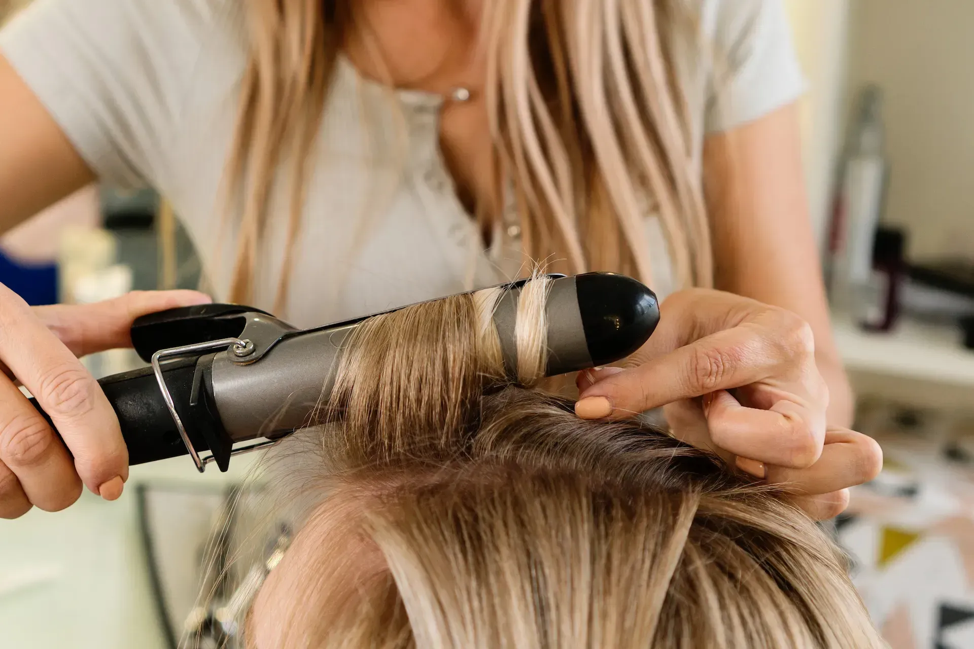 Peluquera rizando el cabello rubio de una clienta con un rizador.