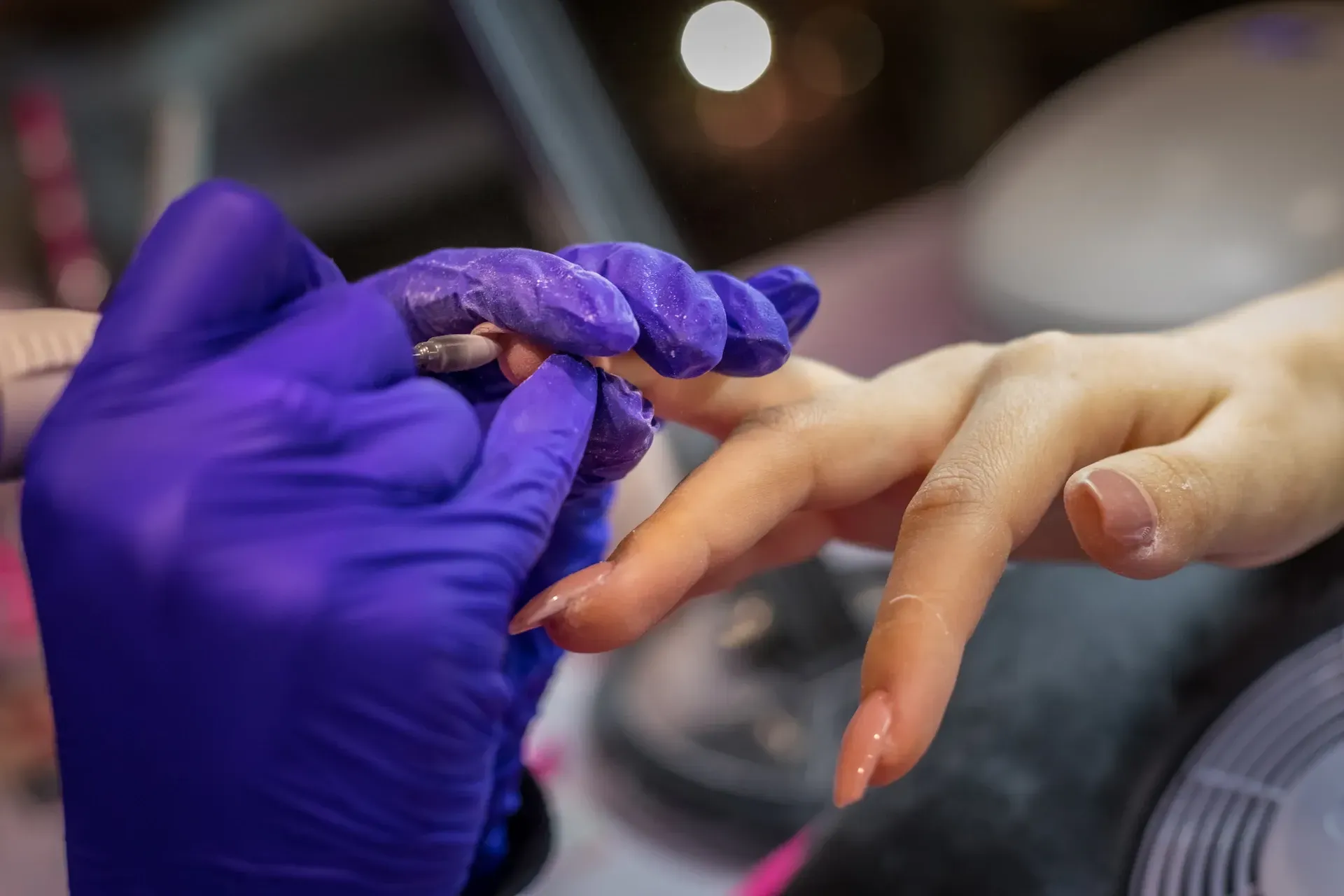Las manos enguantadas de una manicurista aplican esmalte de uñas en las uñas largas y desnudas de una clienta en un salón.