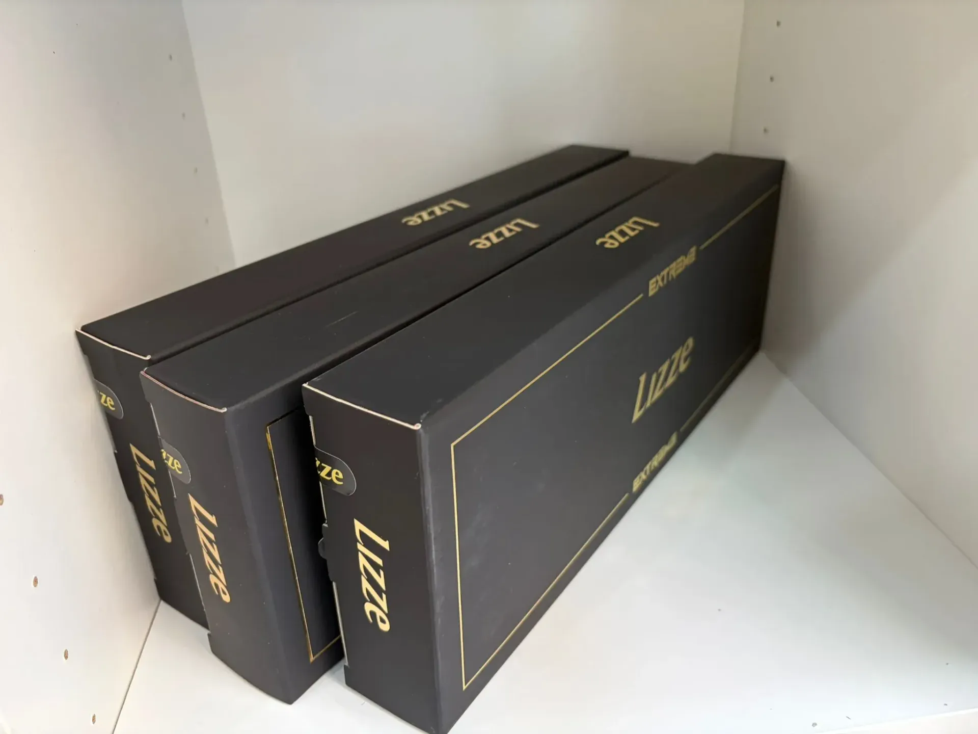 Tres cajas negras con letras doradas, apiladas en un estante blanco. Se ve la palabra 