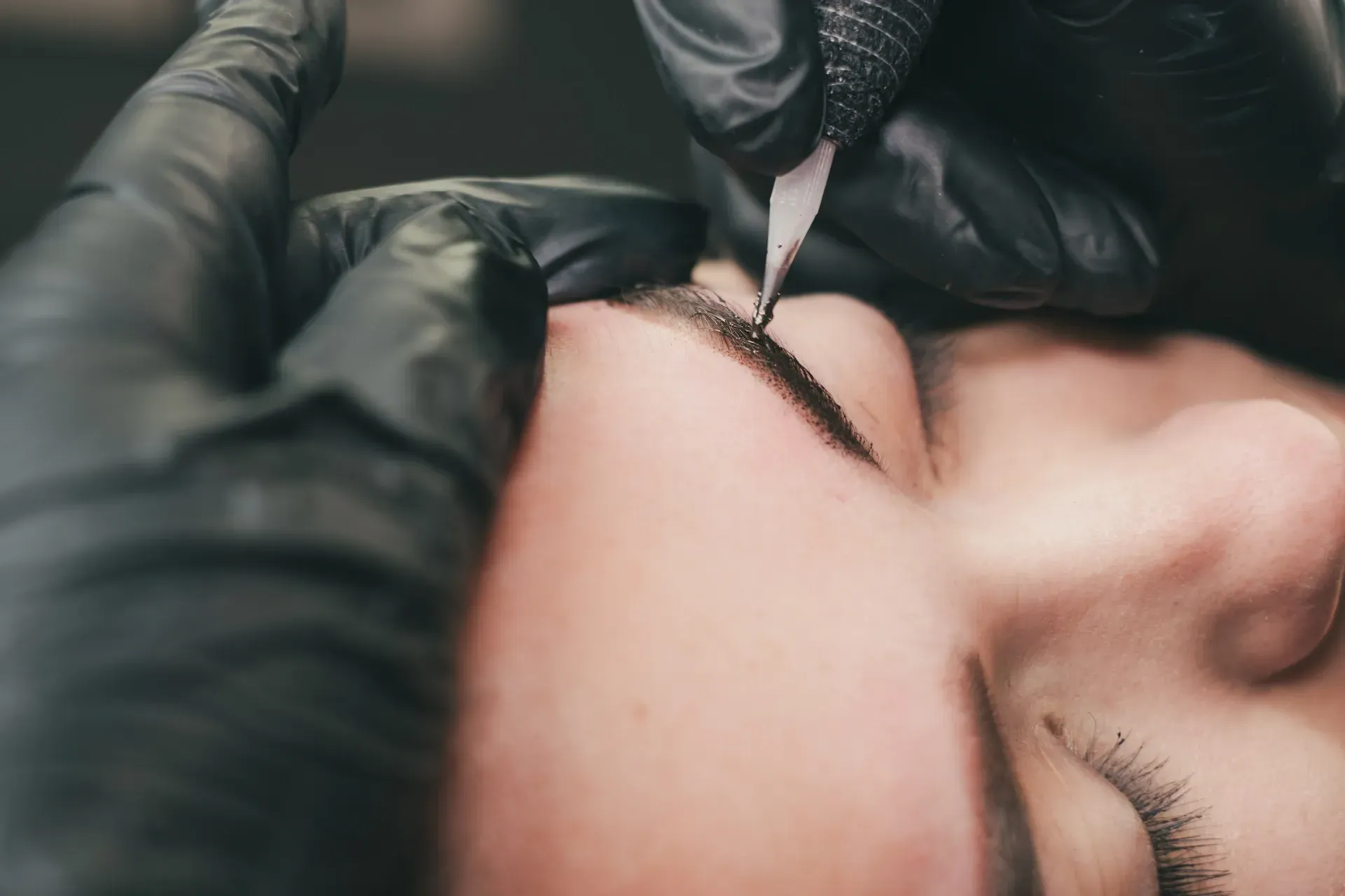 Manos con guantes negros realizando microblading en una ceja.