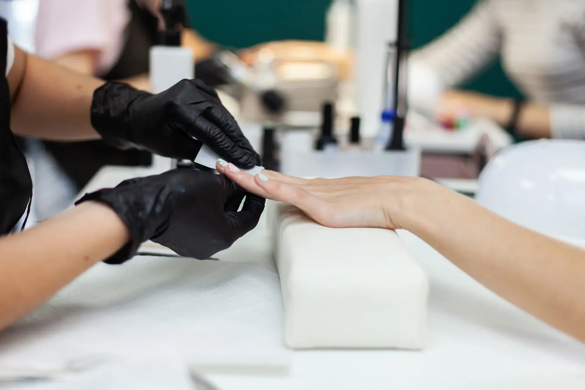 Manicurista con guantes negros aplicando esmalte de uñas en la mano de una clienta en un salón.