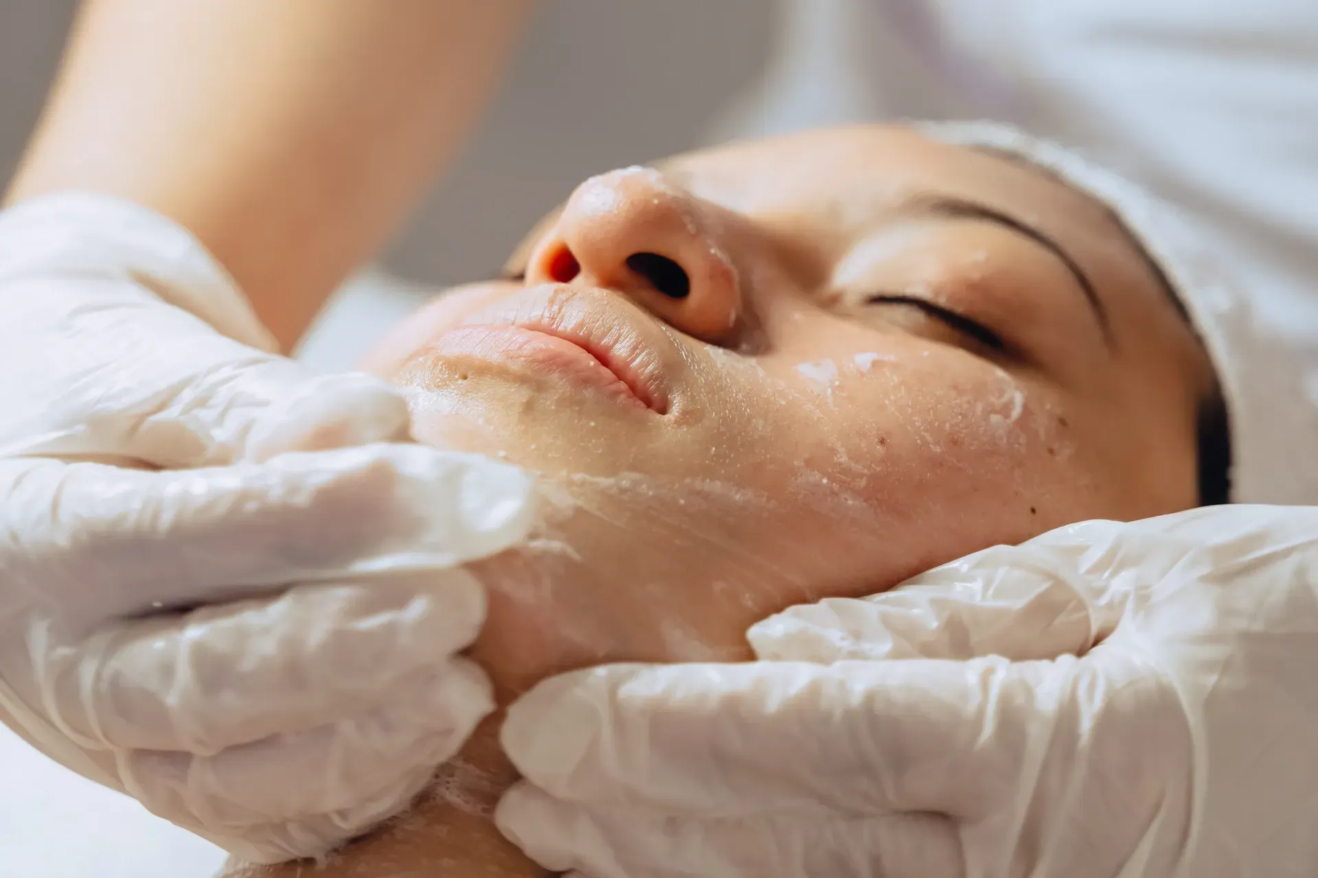 Persona recibiendo tratamiento facial, manos en guantes masajeando suavemente la cara.