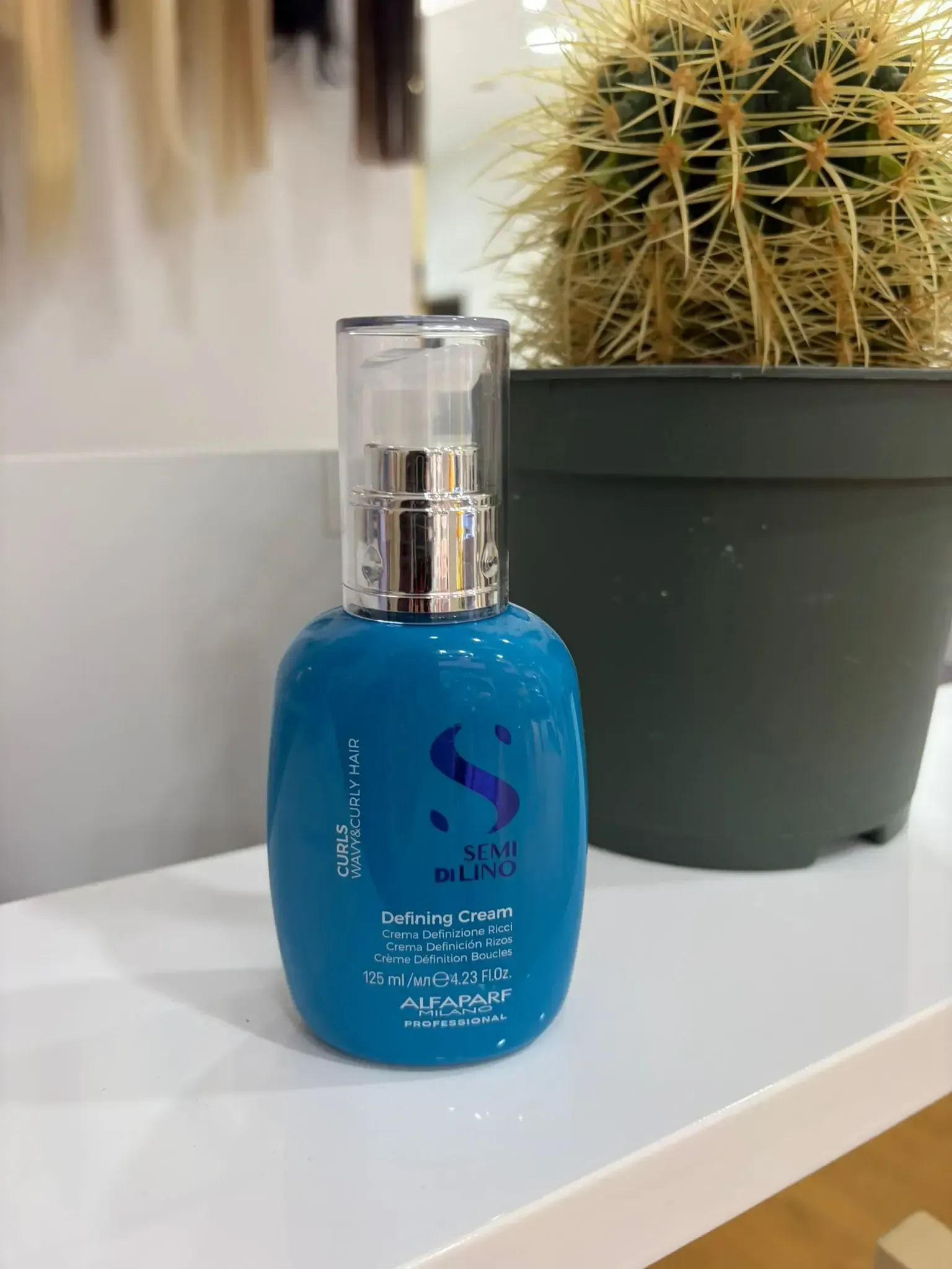 Botella de suero para cabello azul con dispensador de bomba, junto a un cactus en una maceta  sobre una superficie.