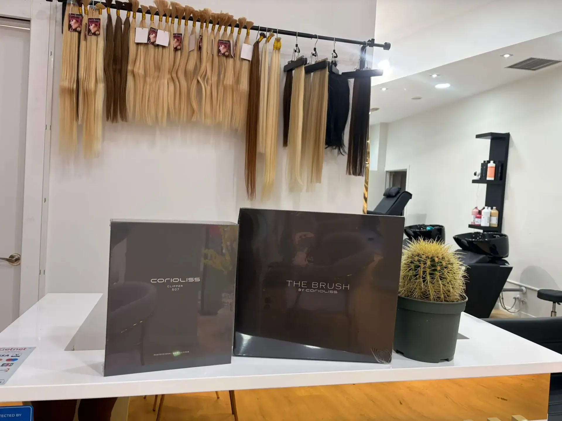 Extensiones de cabello en exhibición en un salón, con cajas y un cactus en un mostrador.