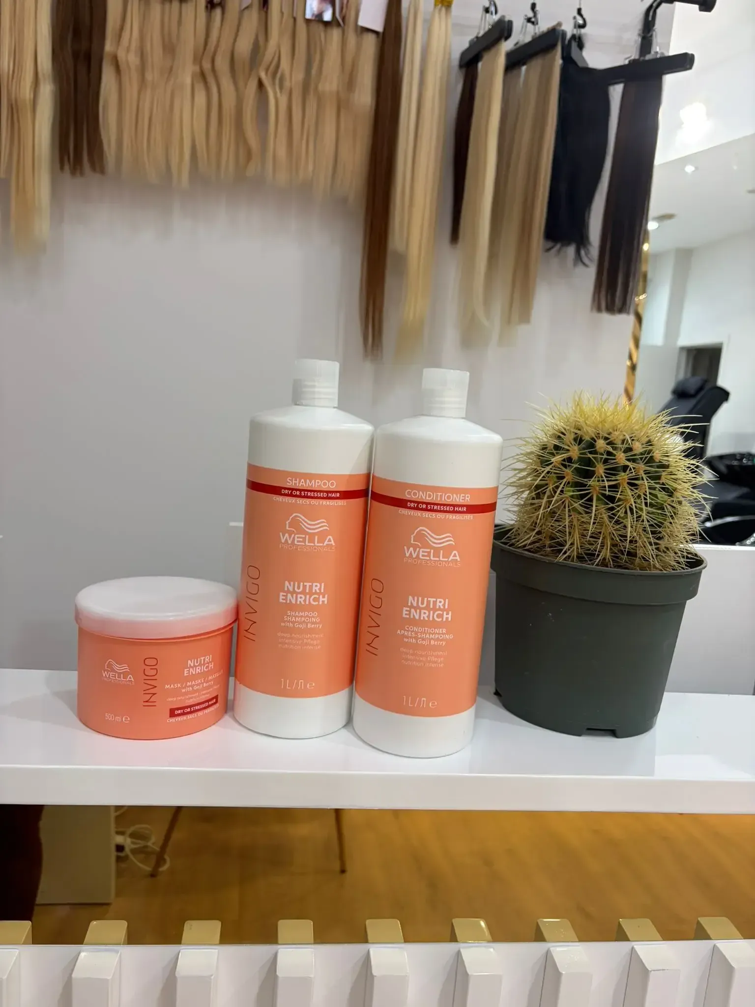 Productos para el cuidado del cabello y cactus en un estante con extensiones de cabello al fondo.