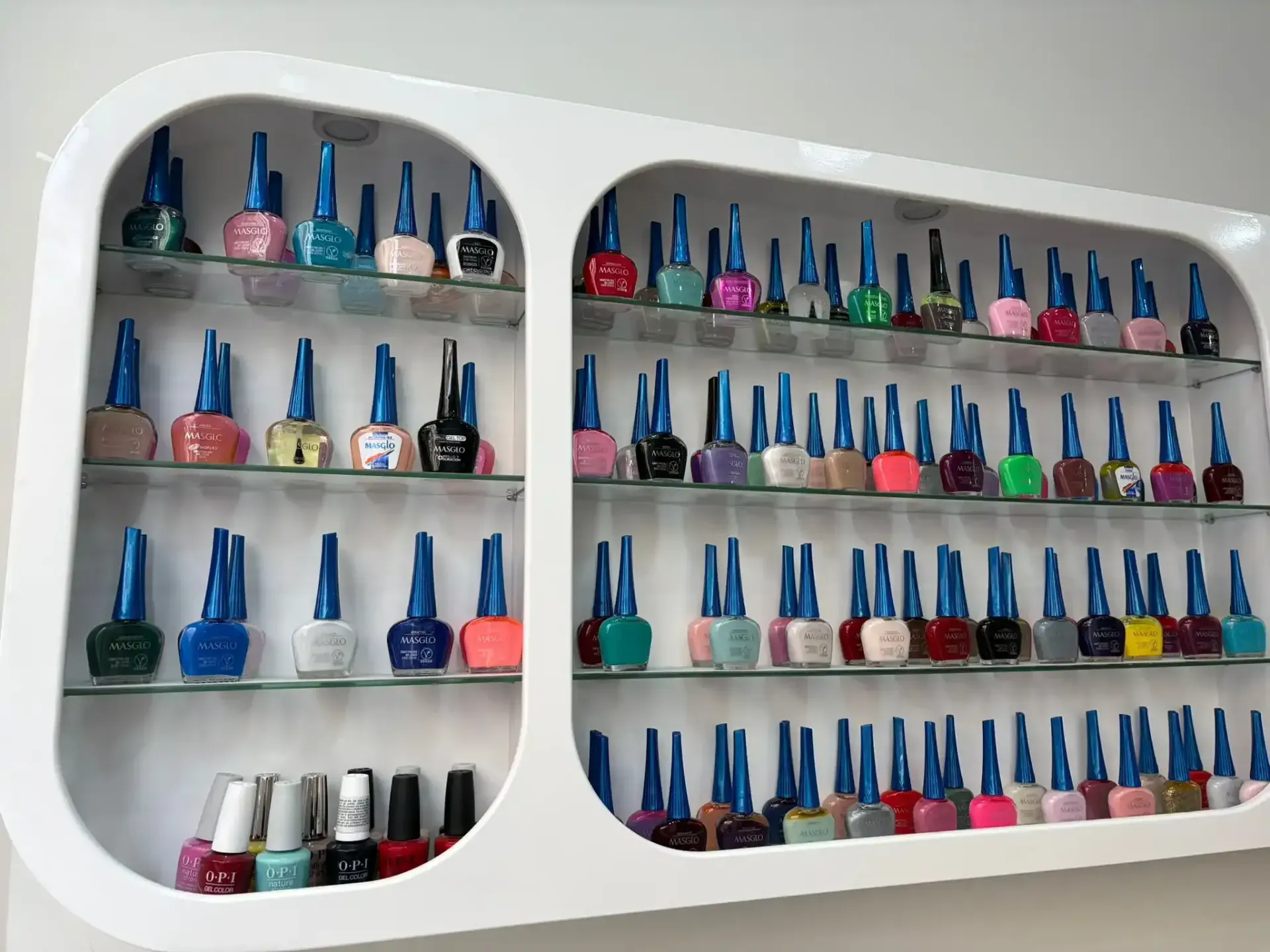 Estante de exhibición blanco lleno de varias botellas de esmalte de uñas.