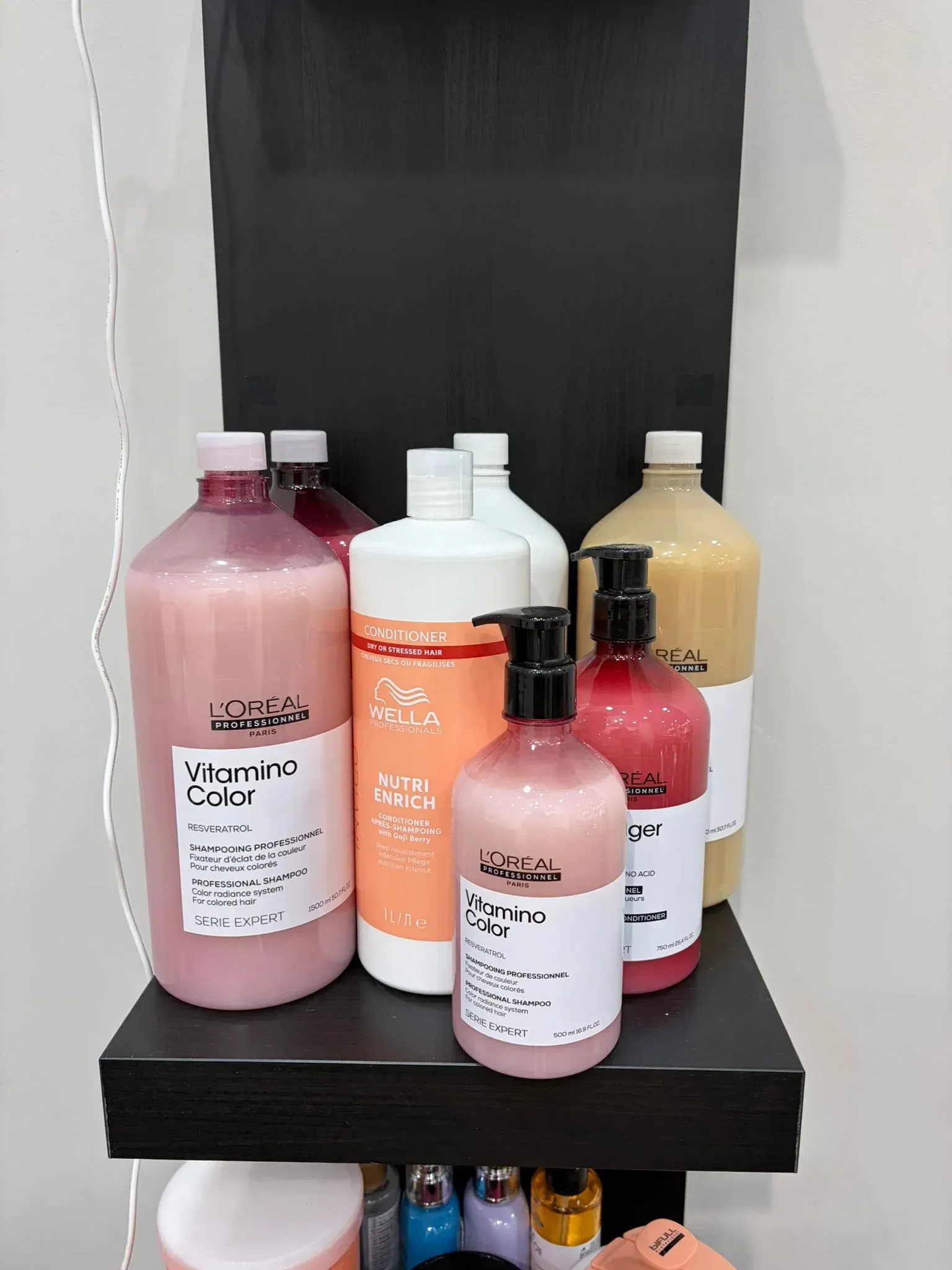 Botellas de champú y acondicionador de varios colores en un estante negro contra una pared.