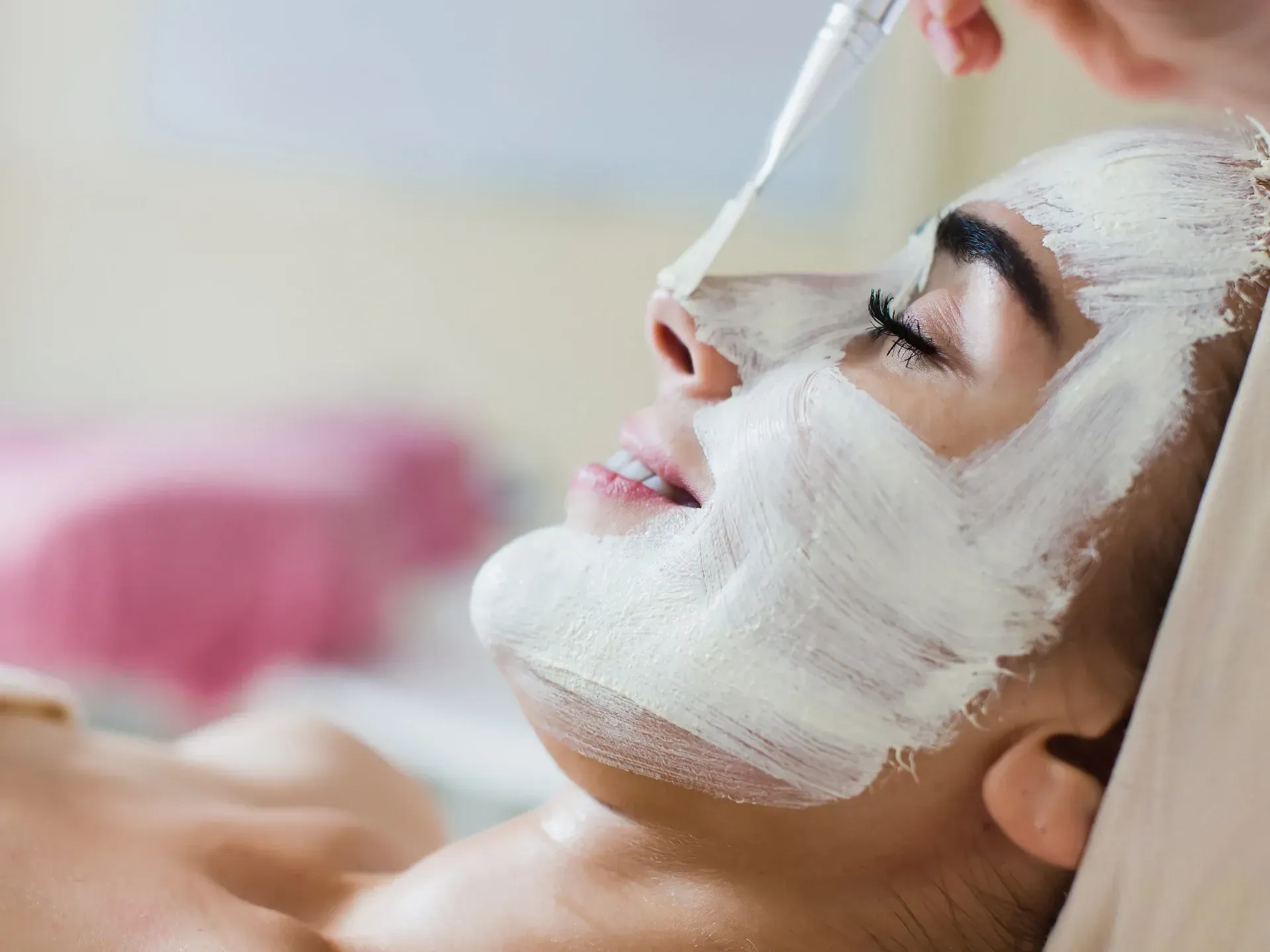 Persona que recibe un tratamiento con mascarilla facial en un spa, con una mascarilla blanca aplicada en el rostro.