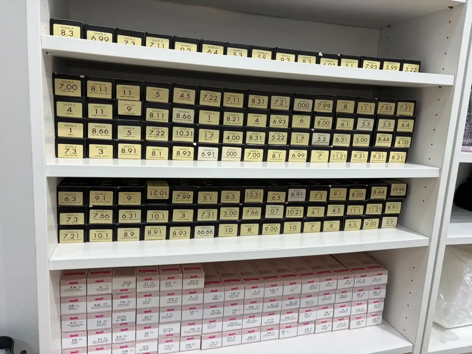 Estantes llenos de contenedores negros numerados y filas de cajas blancas con etiquetas rosas.