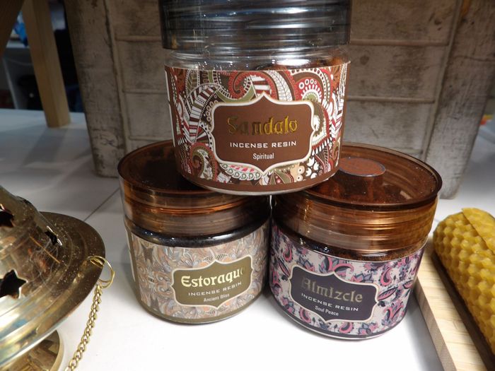 Tres frascos de velas aromáticas ornamentados apilados en un estante, con maíz y un objeto decorativo dorado cerca.