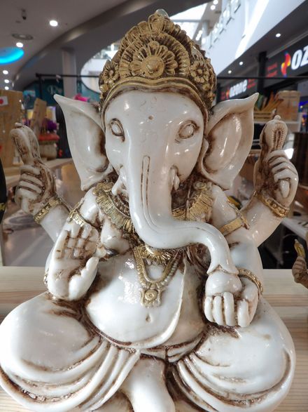 Estatua de Ganesha blanca y dorada sentada en un centro comercial, con corona y joyas ornamentadas.