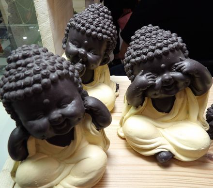 Tres pequeñas figuritas de Buda con cabezas negras y túnicas color crema, sentadas sobre una superficie de madera.