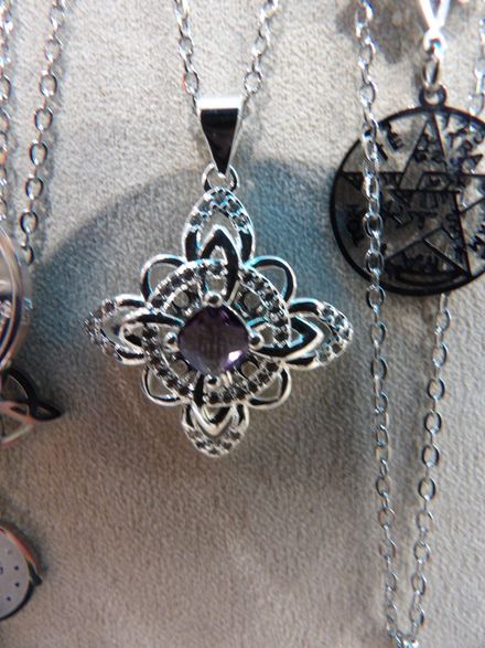 Collar con colgante de plata con una gema morada en forma de corazón sobre un fondo beige.