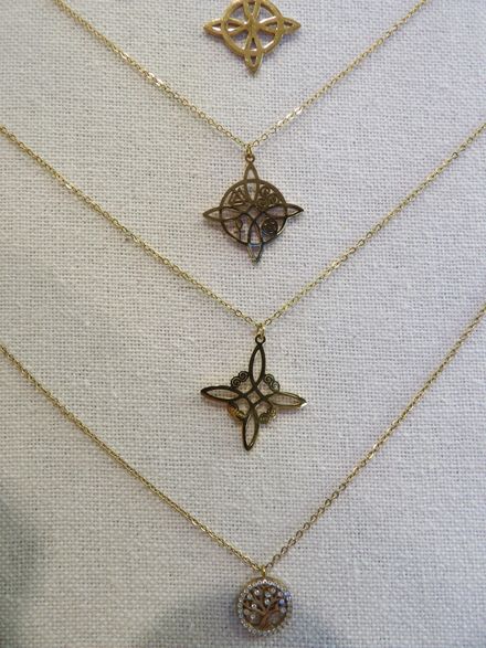 Cuatro collares de oro con colgantes geométricos expuestos sobre un fondo blanco texturizado.