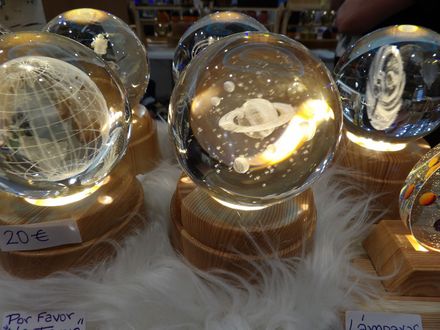 Bolas de cristal sobre soportes de madera en un puesto de mercado, con etiquetas de precio escritas a mano e iluminación cálida.