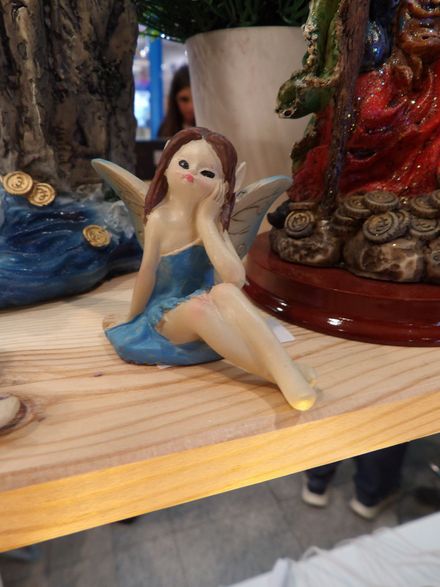 Pequeña figurita de hada con vestido azul sentada en un estante de madera entre objetos decorativos.