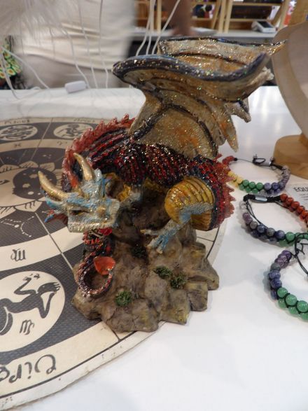 Escultura de dragón colorida hecha con cuentas sobre una mesa junto a una alfombra cubierta de cuentas y collares de joyas.