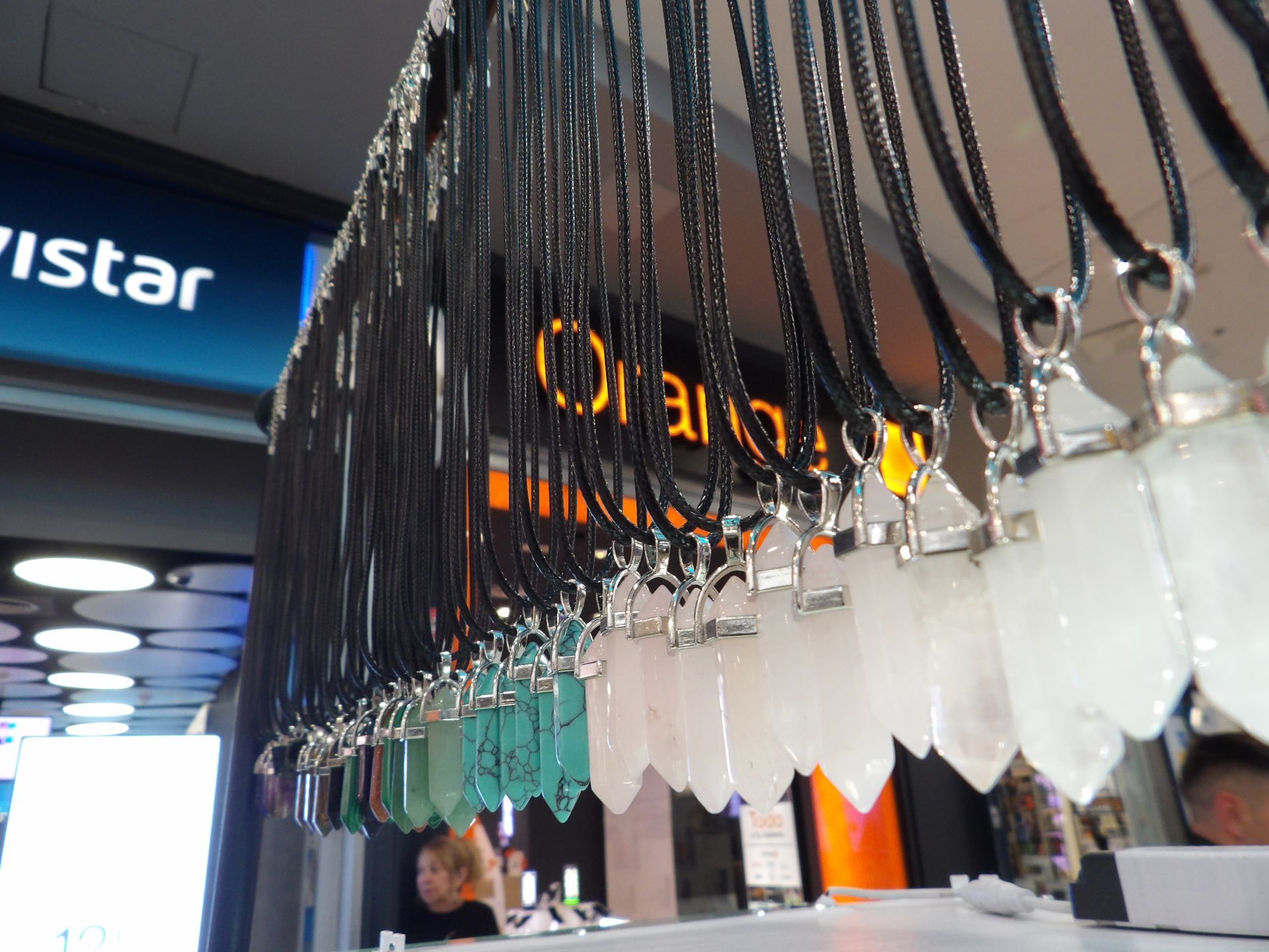 Filas de piezas colgantes de vidrio o plástico transparente en el interior de una tienda, con letreros naranjas al fondo.