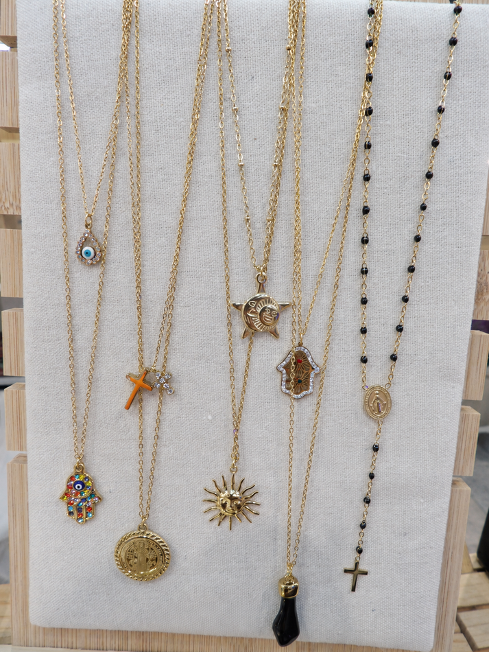 Surtido de collares de oro y cuentas expuestos en una pizarra blanca, incluyendo colgantes, cruces y diseños de dijes.