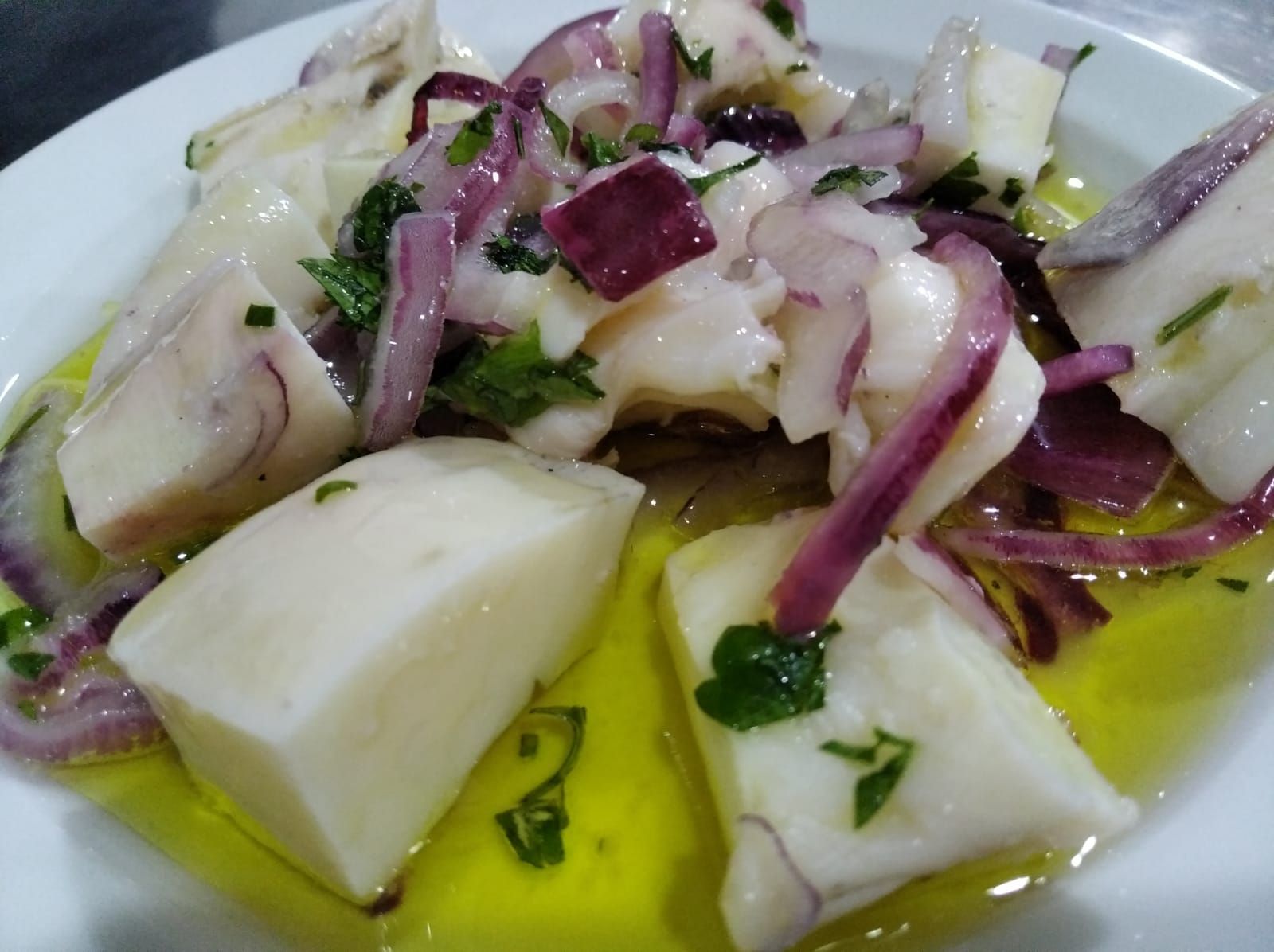 Ensalada de pescado blanco con cebolla roja y perejil en aceite de oliva.