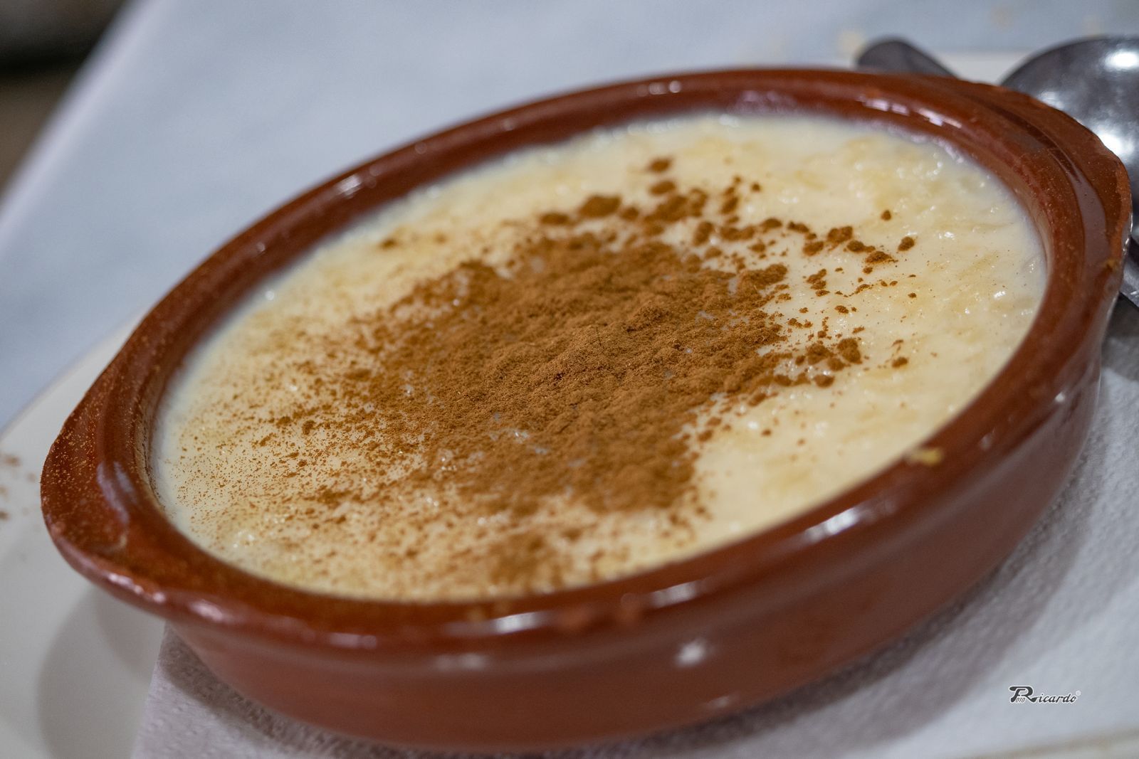 Arroz con leche en un recipiente marrón, espolvoreado con canela.
