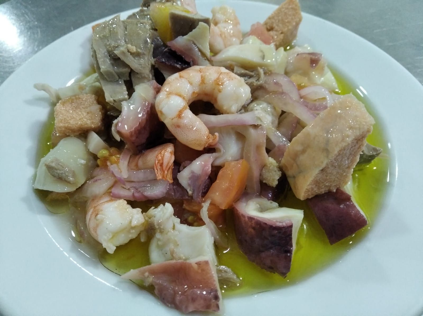 Ensalada de mariscos en plato blanco, con pulpo, camarones y un chorrito de aceite de oliva.
