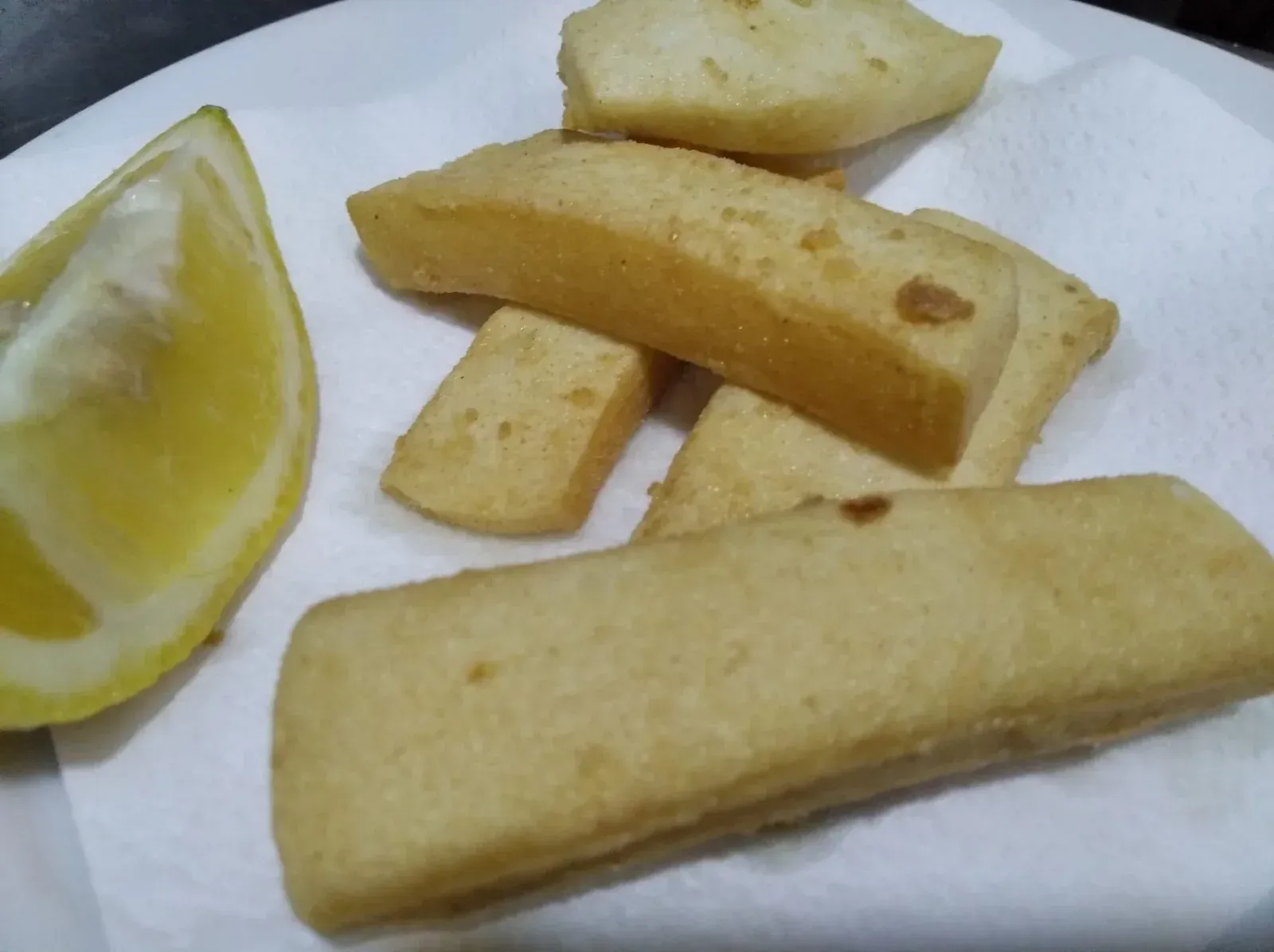 Rectángulos de queso frito con una rodaja de limón en un plato blanco.