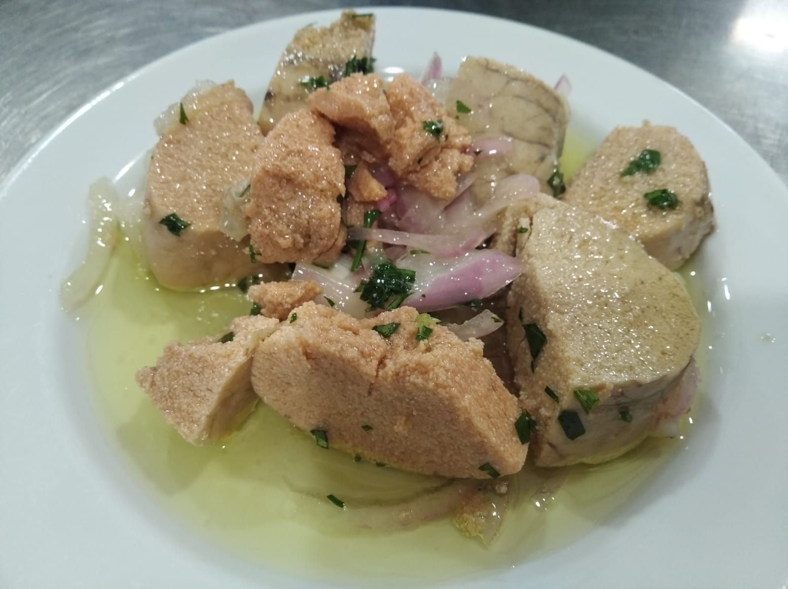 Plato de pescado cortado en rodajas de color claro, con huevas de color marrón rojizo y cebollas rojas en un charco de aceite.