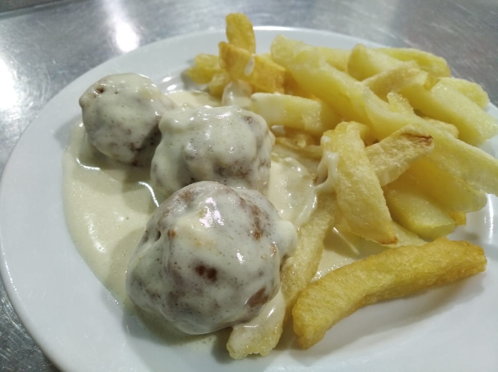 Albóndigas en salsa cremosa con patatas fritas en un plato blanco.