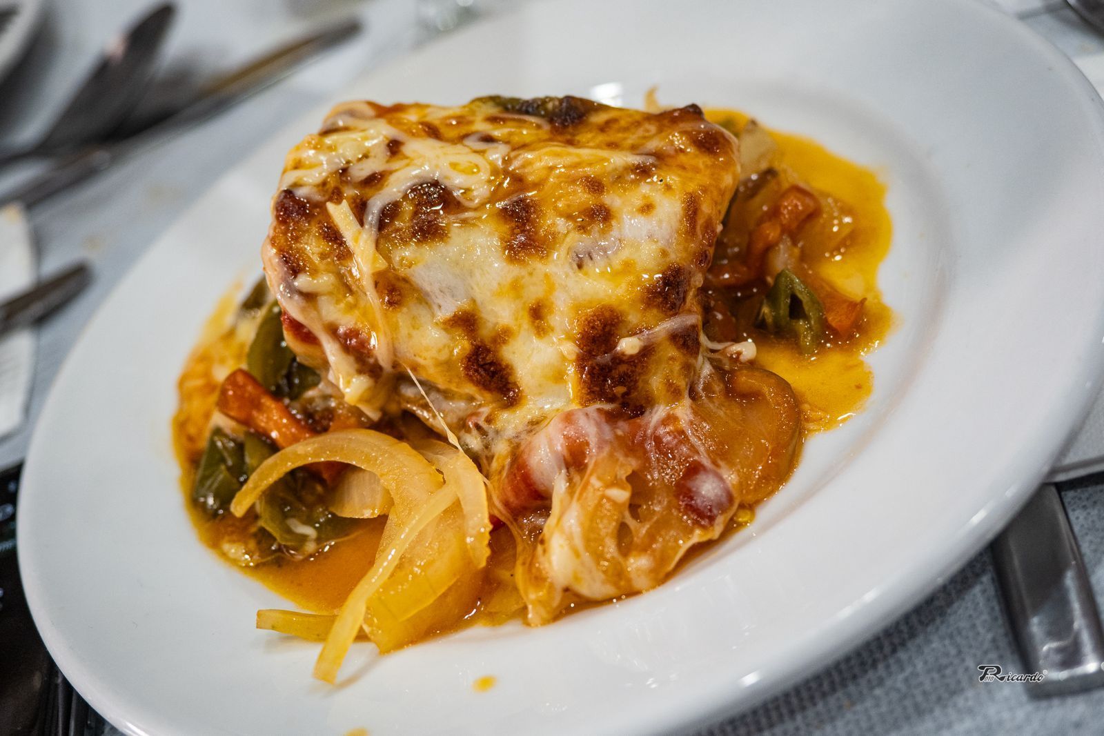 Pescado al horno con queso y verduras en un plato blanco.