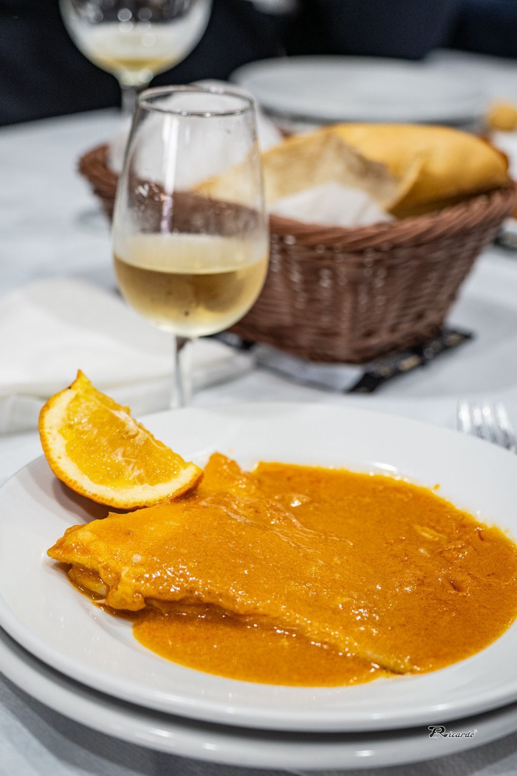 Plato de comida con salsa de naranja, con rodaja de naranja, vino blanco y cesta de pan.