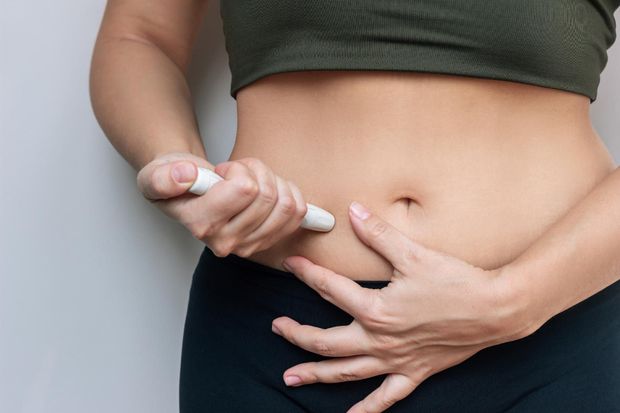 Person in Schutzkleidung und Handschuhen, die in einem Labor ein Mikroskop benutzt.