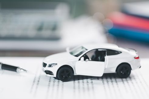 Un sedán de juguete blanco con la puerta abierta sobre un escritorio junto a un bolígrafo y un cuaderno.