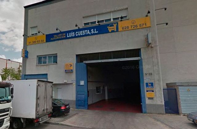 Entrada a un almacén industrial con puerta azul, letrero de la empresa y camión blanco estacionado.