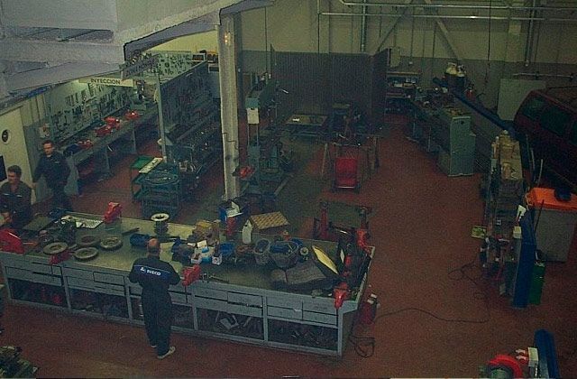 Cocina industrial interior con trabajadores preparando alimentos alrededor de encimeras y equipos de acero inoxidable.