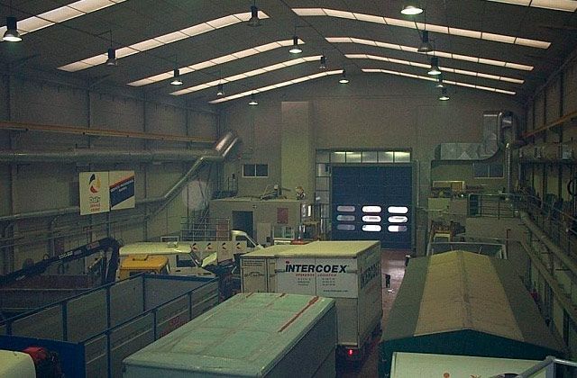 Interior de almacén con camiones, luces de techo altas y una gran puerta de carga abierta.