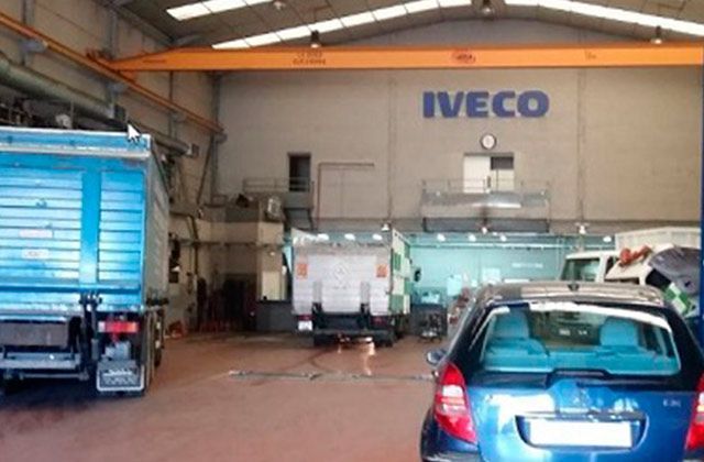 Interior del garaje con vehículos estacionados y un letrero de IVECO en la pared.