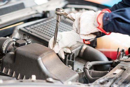 Mecánico utilizando una llave inglesa para reparar un motor de coche abierto en un garaje.