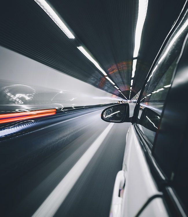 Voiture blanche filant à toute allure dans un tunnel, traînées lumineuses et reflets flous.